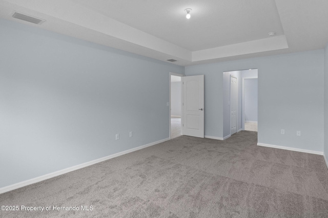 unfurnished room featuring a raised ceiling, carpet, visible vents, and baseboards