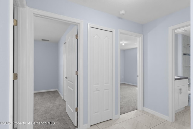 corridor featuring visible vents, light carpet, baseboards, and light tile patterned flooring