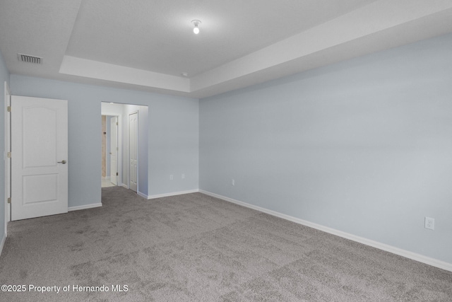 unfurnished room with a raised ceiling, carpet, visible vents, and baseboards