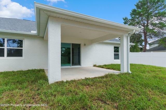 rear view of property featuring a patio, fence, roof with shingles, stucco siding, and a lawn