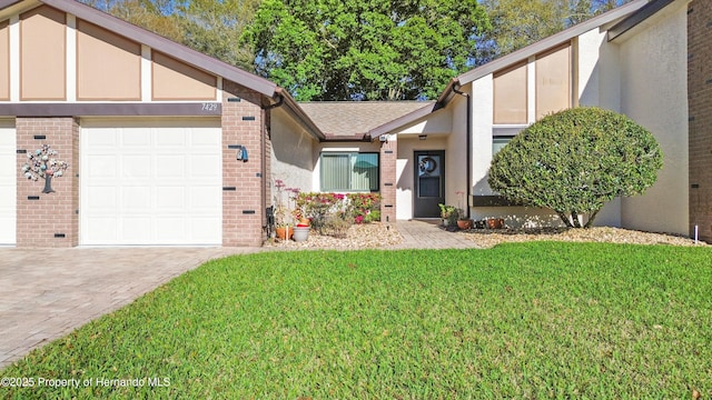 view of front of property featuring a front yard, roof with shingles, an attached garage, decorative driveway, and brick siding