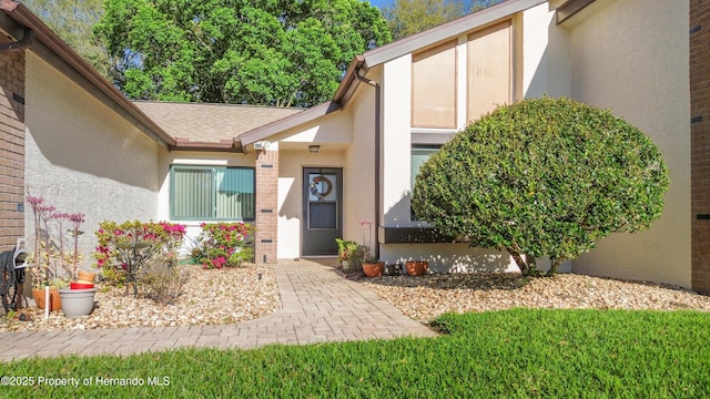 property entrance with stucco siding and a shingled roof