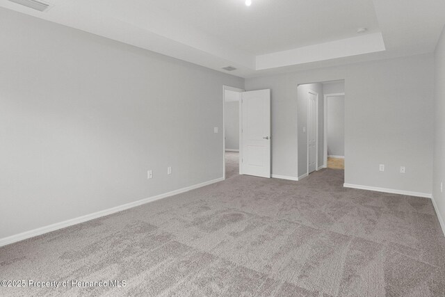 unfurnished bedroom with a tray ceiling, baseboards, visible vents, and carpet flooring