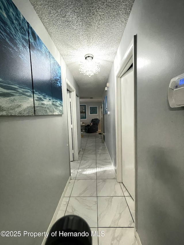 hall with marble finish floor, a textured ceiling, and baseboards