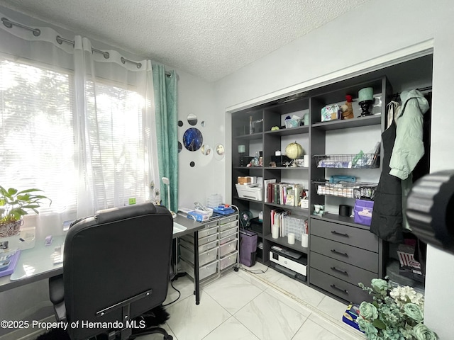 home office featuring marble finish floor, a textured ceiling, and a healthy amount of sunlight