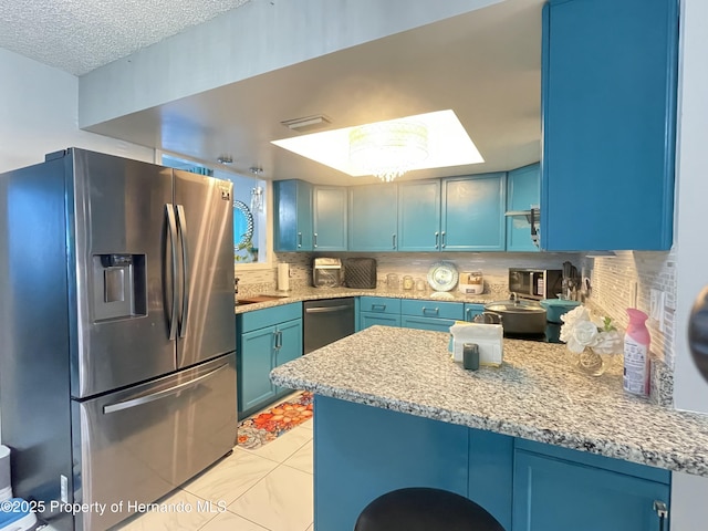 kitchen with decorative backsplash, blue cabinetry, appliances with stainless steel finishes, and a peninsula