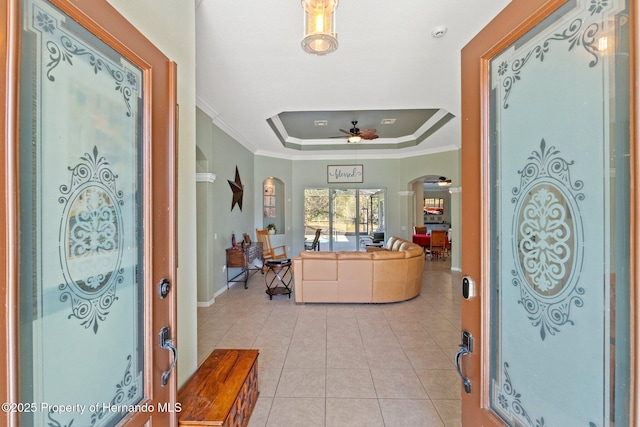 entryway with a ceiling fan, a tray ceiling, arched walkways, light tile patterned flooring, and crown molding