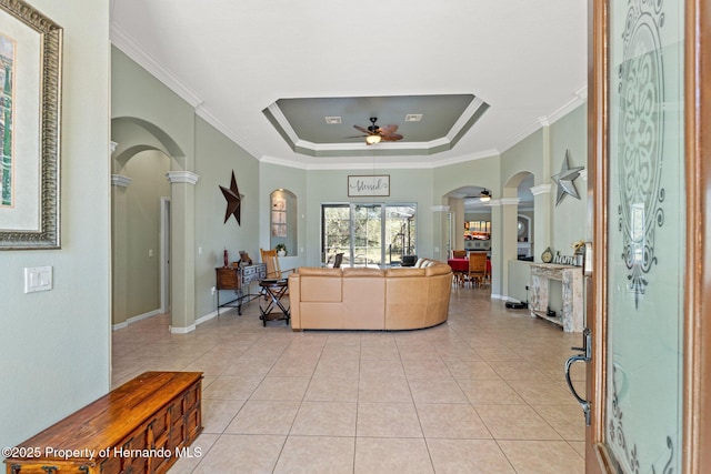 living area featuring arched walkways, a raised ceiling, a ceiling fan, and decorative columns