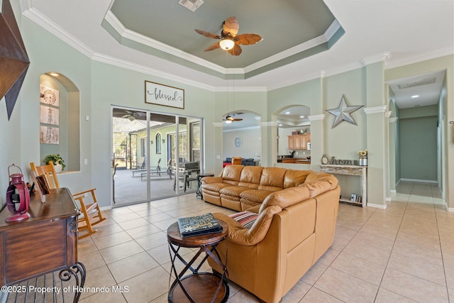 living room featuring arched walkways, a ceiling fan, a tray ceiling, and ornate columns