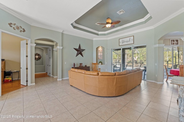 living area featuring a ceiling fan, arched walkways, light tile patterned flooring, decorative columns, and a raised ceiling