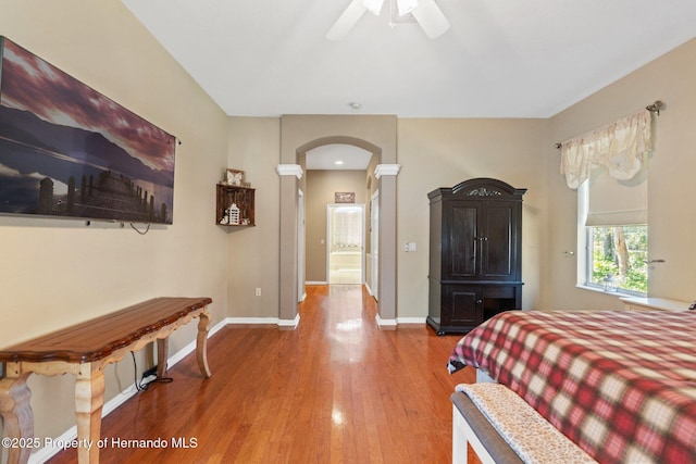 bedroom featuring ceiling fan, baseboards, wood finished floors, arched walkways, and ornate columns