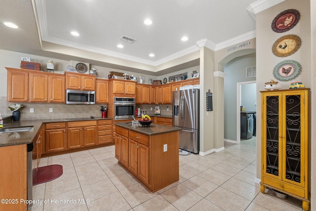 kitchen featuring arched walkways, appliances with stainless steel finishes, a raised ceiling, and a kitchen island with sink