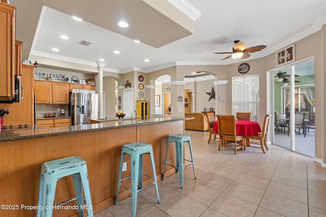 kitchen featuring stainless steel fridge with ice dispenser, a breakfast bar, ornamental molding, arched walkways, and a ceiling fan