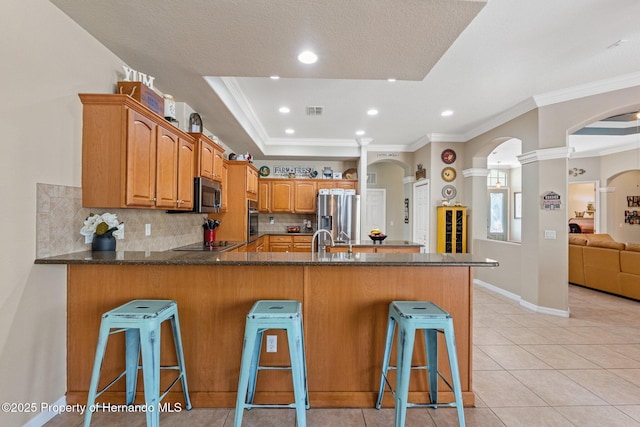 kitchen with a peninsula, arched walkways, stainless steel appliances, a raised ceiling, and a kitchen breakfast bar