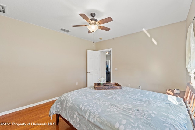 bedroom featuring ceiling fan, visible vents, baseboards, and wood finished floors