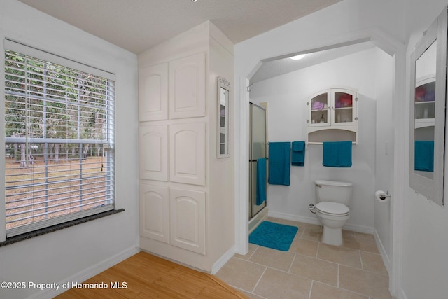 full bathroom featuring tile patterned flooring, a stall shower, toilet, and baseboards