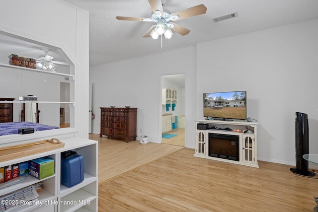 living area featuring wood finished floors, a ceiling fan, visible vents, and a textured ceiling
