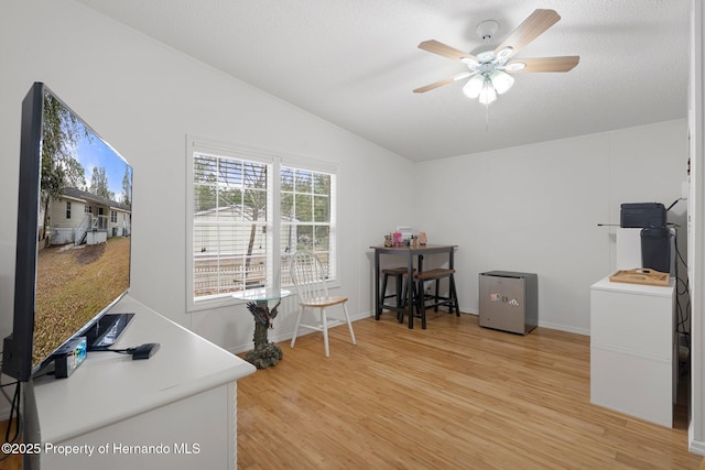 office area with baseboards, light wood-type flooring, ceiling fan, and vaulted ceiling