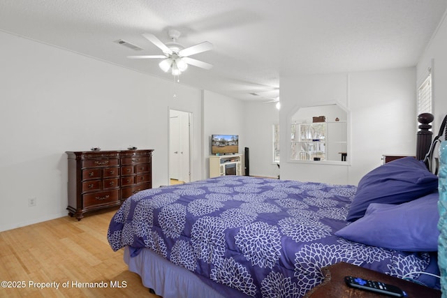 bedroom featuring a ceiling fan, wood finished floors, visible vents, and a textured ceiling