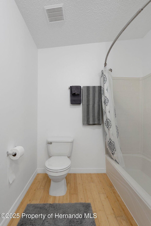 bathroom with wood finished floors, visible vents, shower / bath combo with shower curtain, a textured ceiling, and toilet