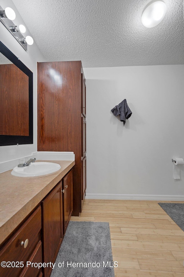 bathroom featuring vanity, wood finished floors, baseboards, and a textured ceiling