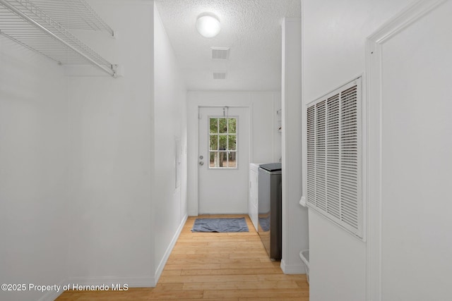 doorway featuring visible vents, a textured ceiling, light wood-style floors, baseboards, and a heating unit