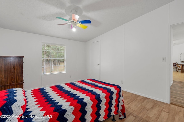 bedroom with a ceiling fan, wood finished floors, baseboards, and a textured ceiling
