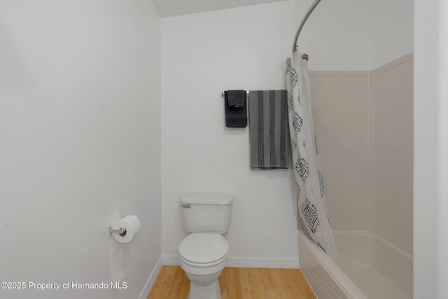 bathroom with shower / bath combo with shower curtain, toilet, wood finished floors, and baseboards