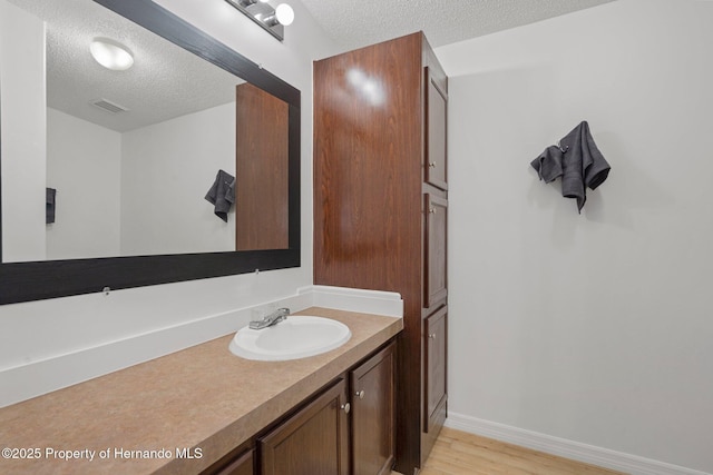 bathroom with vanity, wood finished floors, baseboards, visible vents, and a textured ceiling