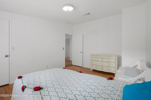 bedroom with visible vents, a textured ceiling, and wood finished floors