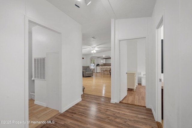 hallway featuring visible vents, baseboards, a textured ceiling, and wood finished floors