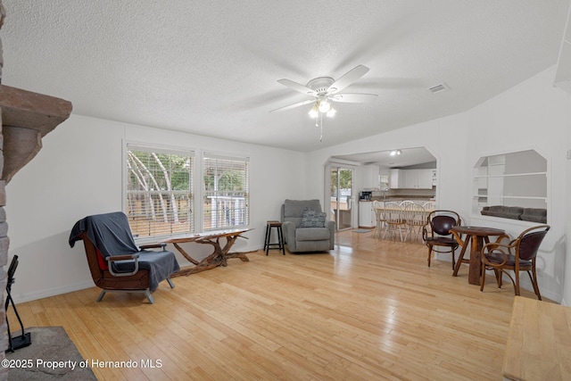 sitting room featuring a ceiling fan, visible vents, light wood finished floors, arched walkways, and a textured ceiling