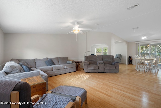 living area with visible vents, light wood finished floors, lofted ceiling, arched walkways, and a textured ceiling