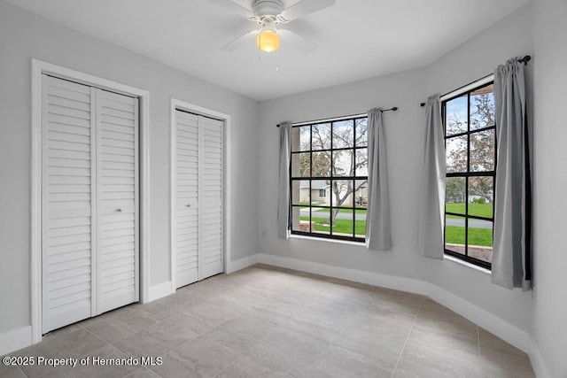 11080 Marquette St, Spring Hill, FL 34609 - unfurnished bedroom with light tile patterned floors, baseboards, ceiling fan, and two closets
