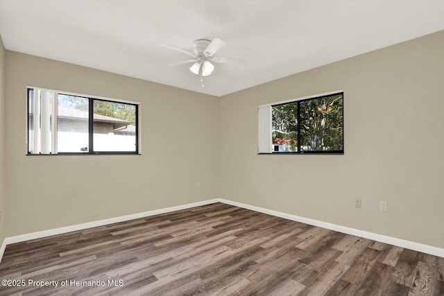 empty room with wood finished floors, a wealth of natural light, a ceiling fan, and baseboards