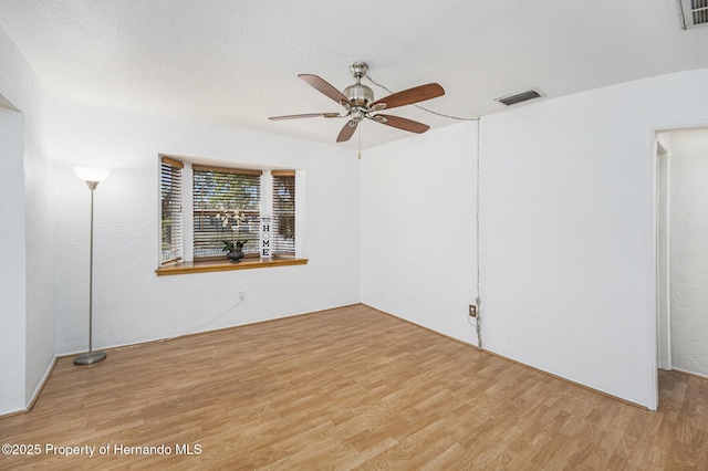 empty room with a textured ceiling, visible vents, wood finished floors, and a ceiling fan