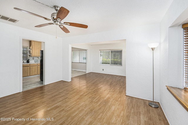 unfurnished living room with a textured ceiling, visible vents, light wood-style floors, and a ceiling fan