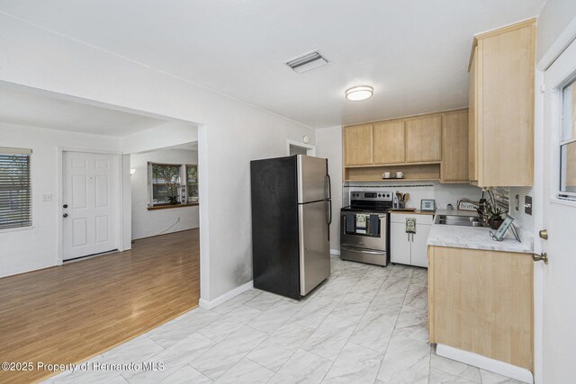 kitchen featuring light countertops, stainless steel appliances, light brown cabinetry, marble finish floor, and a sink