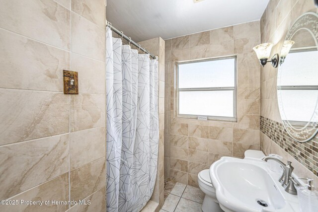 bathroom with tile walls, toilet, tile patterned floors, curtained shower, and a sink