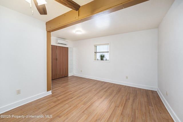 unfurnished room with a wall unit AC, beam ceiling, baseboards, and light wood-type flooring