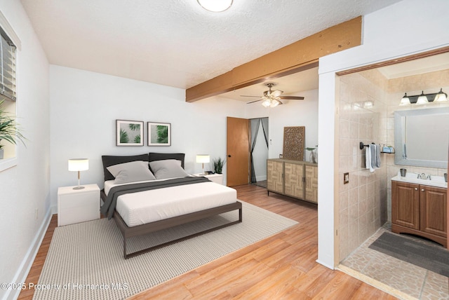 bedroom with beam ceiling, a sink, a textured ceiling, baseboards, and light wood-style floors