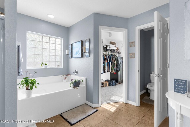 1018 Stratton Ave, Spring Hill, FL 34609 - bathroom with toilet, a garden tub, a walk in closet, tile patterned flooring, and baseboards