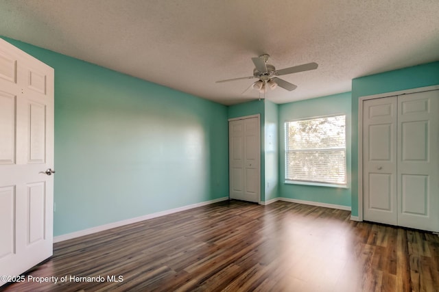unfurnished bedroom with multiple closets, a textured ceiling, baseboards, a ceiling fan, and dark wood-style floors