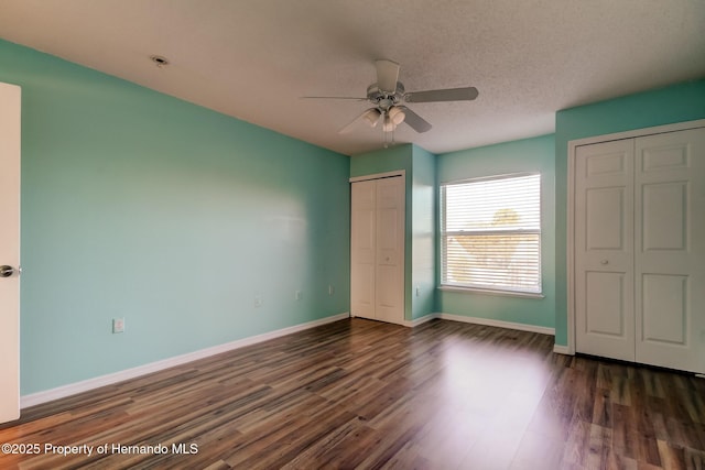 unfurnished bedroom featuring wood finished floors, a textured ceiling, baseboards, two closets, and ceiling fan