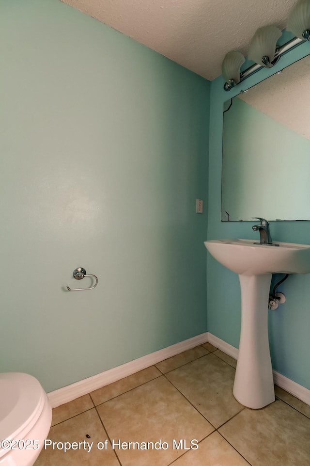 bathroom with baseboards, a textured ceiling, toilet, and tile patterned flooring