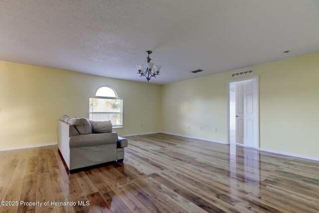 sitting room with an inviting chandelier, baseboards, a textured ceiling, visible vents, and wood finished floors