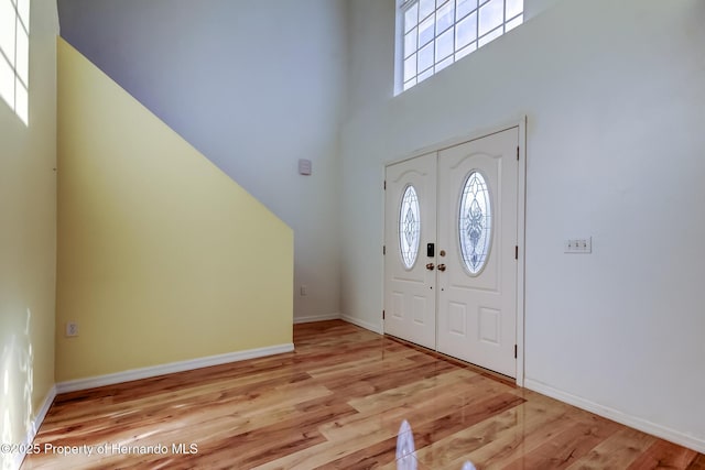 entryway with baseboards, a towering ceiling, wood finished floors, and plenty of natural light