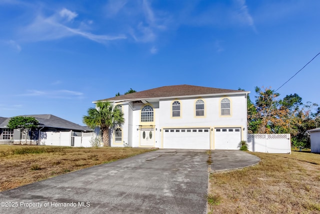 view of front facade with driveway, fence, an attached garage, a front lawn, and stucco siding