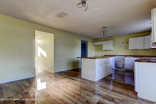 kitchen with white cabinetry, dark countertops, visible vents, a notable chandelier, and wood finished floors