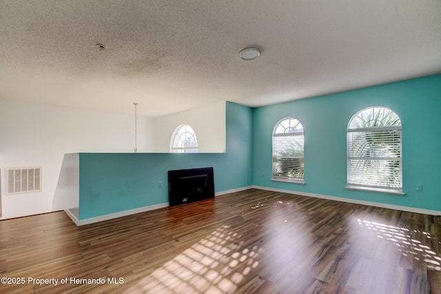 unfurnished living room with a textured ceiling, visible vents, baseboards, a fireplace, and wood finished floors